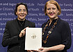Professor of Sociology Michaela Kreyenfeld and Family Affairs Minister Lisa Paus holds up a white paper with a golden eagle on it. They stand in front of a dark blue background.