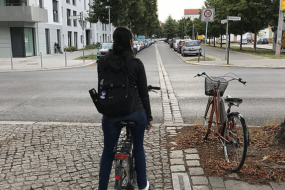 A person sitting on a bike with a backpack on a cobblestone street.