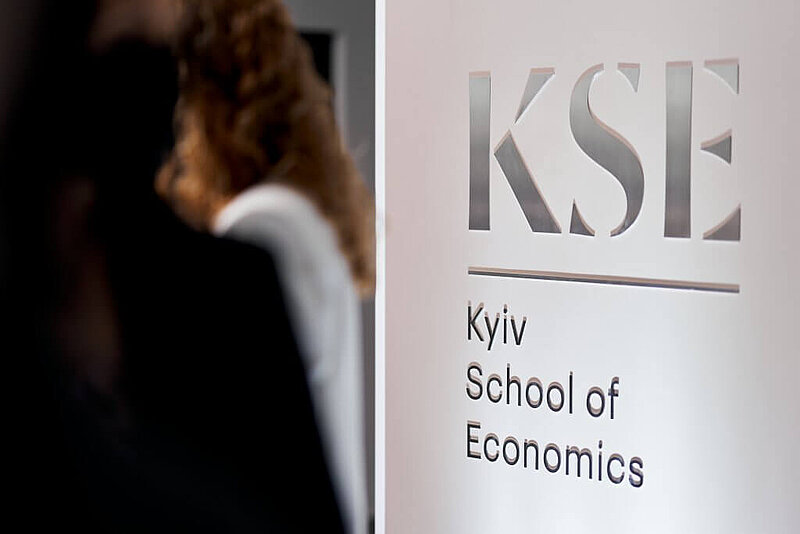 The Kyiv School of Economics logo and name in silver on a white wall. Photo source: Kyiv School of Economics.
