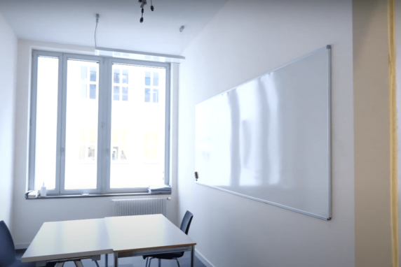 Small study room with a white table and chairs, with a window in the background and a whiteboard on the wall to the right