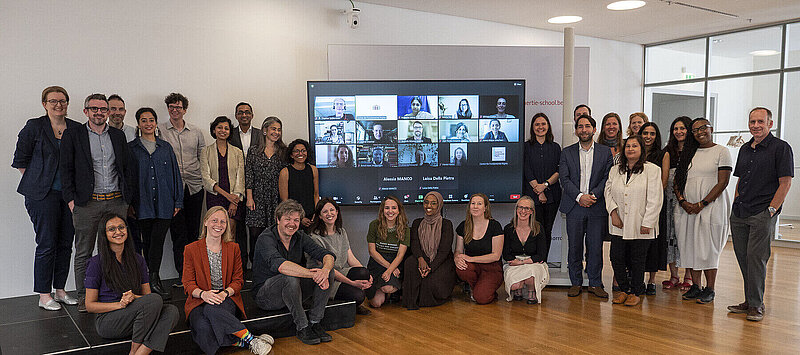 Online and on-site participants in the Hertie School Centre for Fundamental Rights workshop "Decolonising Global Migration Law" gather for a photo in the Hertie School Forum. Online participants are displayed on a large screen.
