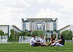 Four people sitting on green grass in front of Berlin government building Bundeskanzleramt.