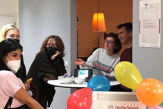 Members represent the Hertie School Pride Network at the spring 2022 club fair on campus. Colorful balloons adorn the club week sign.