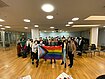 The Hertie School Pride Network and trans German Member of Parliament Nyke Slawik hold up the Progress Pride Flag in the Hertie School Forum in front of a large crowd.